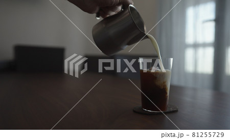 pour milk over cold brew coffee over ice cube in tumbler glass on walnut table 81255729