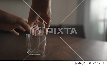 man put ice ball into tumbler gllass on walnut table 81255734