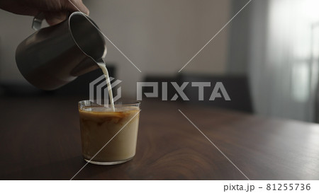 pour milk into cold brew coffee over ice ball in tumbler glass on walnut table 81255736