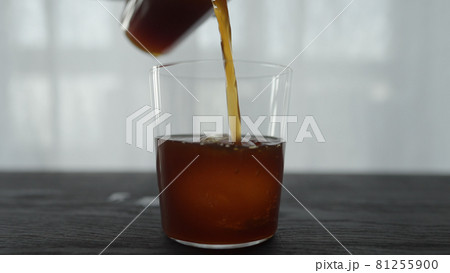pour cold brew coffee over ice ball in tumbler glass on wood table 81255900