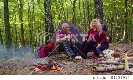 Senior grandmother grandfather granddaughter telling funny stories fairy tales over campfire in wood Senior grandmother grandfather granddaughter telling funny stories fairy tales over campfire in wood 81255914