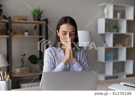 Superstitious young woman worker pray at workplace 81256186