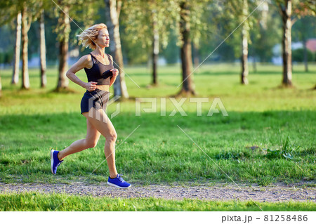 Slim woman in sportswear runs in park. 81258486