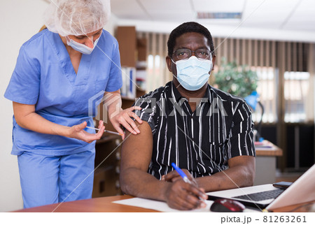 Male nurse injecting vaccine in shoulder of male patient during covid vaccination in office Male nurse injecting vaccine in shoulder of male patient during covid vaccination in office 81263261
