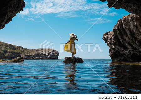 A woman in a white dress and a black hat standing on the rocks by the sea A woman in a white dress and a black hat standing on the rocks by the sea 81263311