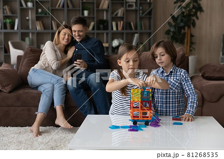 Kids play constructor while parents use smartphone seated on sofa Kids play constructor while parents use smartphone seated on sofa 81268535
