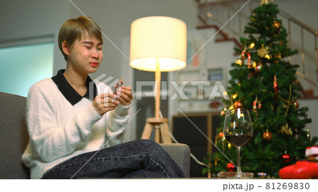 Young woman wears Santa hat eating chocolate on sofa at home during coronavirus quarantine long distance celebration. Young woman wears Santa hat eating chocolate on sofa at home during coronavirus quarantine long distance celebration. 81269830