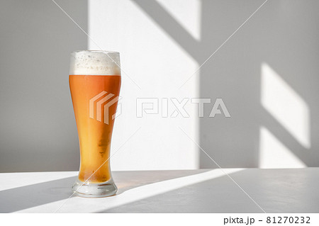 Glass beer on table against white wall with shadows Glass beer on table against white wall with shadows 81270232