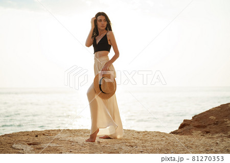 Young stylish woman standing on cliff at the sea at sunset 81270353