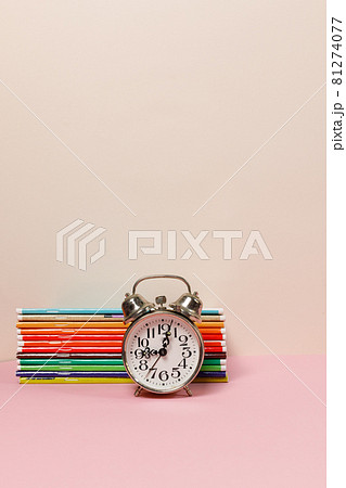 A stack of colorful notebooks and an alarm clock on the table. A vertical frame with space. Pastel colors. 81274077