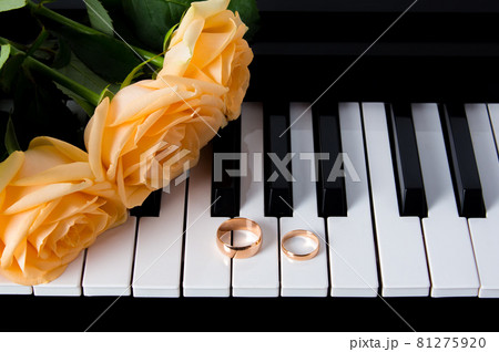 Yellow roses with wedding rings on the piano. Preparing for the wedding. A gift to your beloved for a wedding or Valentine's day. A bouquet of yellow roses lying on the piano with wedding rings. Yellow roses with wedding rings on the piano. Preparing for the wedding. A gift to your beloved for a wedding or Valentine's day. A bouquet of yellow roses lying on the piano with wedding rings. 81275920