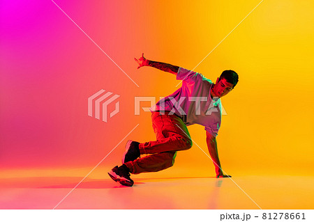 Portrait of young stylish man, break dancing dancer training in casual clothes isolated over gradient pink yellow background at dance hall in neon light. Portrait of young stylish man, break dancing dancer training in casual clothes isolated over gradient pink yellow background at dance hall in neon light. 81278661