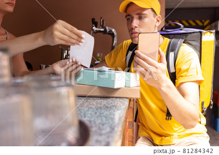 Young deliveryman in yellow uniform picking up order to clients, customers, buyers. Work, career, different professions concept. Idea of convenience, speed, comfort, safety, service. Young deliveryman in yellow uniform picking up order to clients, customers, buyers. Work, career, different professions concept. Idea of convenience, speed, comfort, safety, service. 81284342