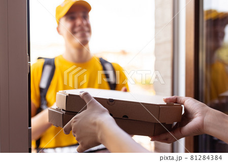 Young deliveryman in yellow uniform delivers order to clients, customers, buyers. Work, career, different professions concept. Idea of convenience, speed, comfort, safety, service. Young deliveryman in yellow uniform delivers order to clients, customers, buyers. Work, career, different professions concept. Idea of convenience, speed, comfort, safety, service. 81284384