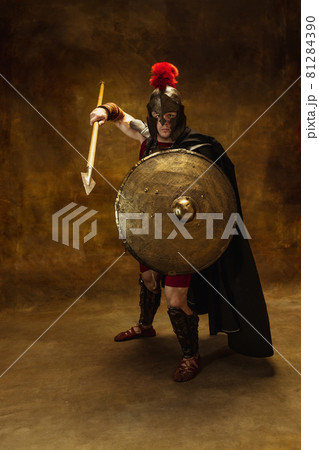 Portrait of medieval person, brutal man, warrior or knight in war equipment isolated on vintage dark background. Comparison of eras, art, history, retro style concept 81284390