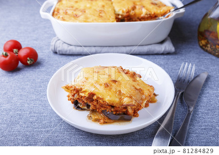 Moussaka with meat, eggplant, tomatoes, potatoes, bechamel sauce and cheese on a white plate. Traditional Greek dish. Close-up. 81284829