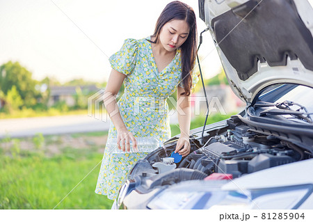 Fixing Her Broken Down Car, a young woman pours a water for washing glasses into her car. Fixing Her Broken Down Car, a young woman pours a water for washing glasses into her car. 81285904