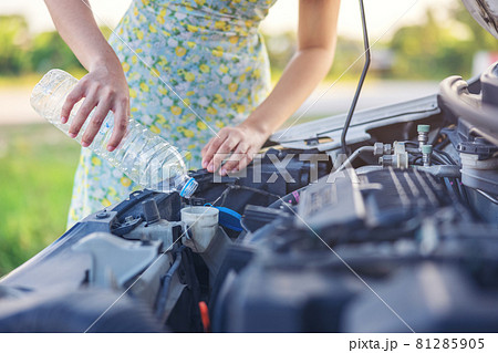 Fixing Her Broken Down Car, a young woman pours a water for washing glasses into her car. 81285905