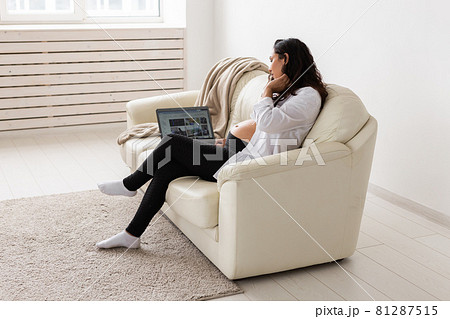 Latin pregnant woman using laptop computer sitting on sofa at home. Pregnancy and information for parenthood concept. Latin pregnant woman using laptop computer sitting on sofa at home. Pregnancy and information for parenthood concept. 81287515