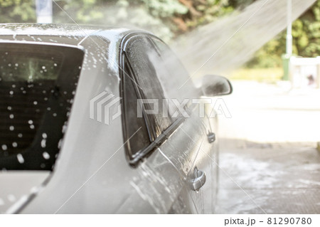 Water spraying from high pressure hose to side window of car washed in self serve carwash. 81290780