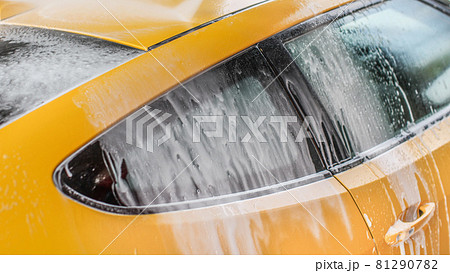 Yellow car washed in self serve carwash, shampoo spraying from hose to roof, streams of foam flowing down the window. Yellow car washed in self serve carwash, shampoo spraying from hose to roof, streams of foam flowing down the window. 81290782