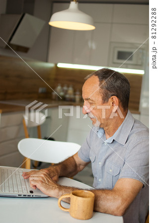 Trendy mature man is working from home with laptop sitting at the table in his kitchen, happy retirement, home-office concepts 81292288
