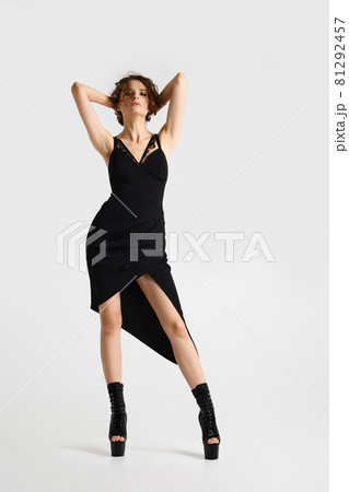 Woman in strap dress with deep cut holds hands behind head 81292457