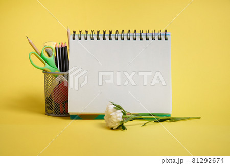 Close-up of a metal bucket with stationery. Holder with colored school supplies, empty blank white paper sheet of an organizer and aster flower lying down on yellow background with copy space 81292674