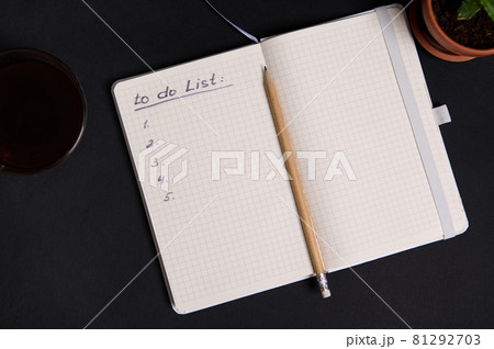 Wooden pencil on the opened agenda, organizer with list to do on blank white sheets, cup of coffee and potted succulent, on black background with copy space 81292703