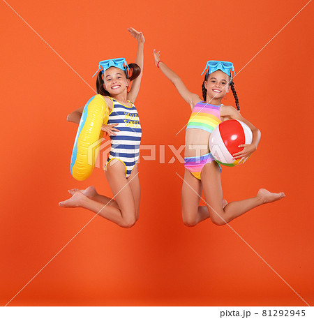 Two funny little sisters in swimsuits and goggles jumping up in air with inflatable swimming ring and ball Two funny little sisters in swimsuits and goggles jumping up in air with inflatable swimming ring and ball 81292945