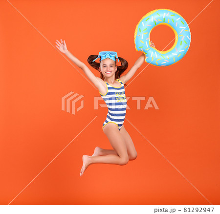 Little funny happy girl in swimsuit and goggles on her head jumping up in air with inflatable ring Little funny happy girl in swimsuit and goggles on her head jumping up in air with inflatable ring 81292947