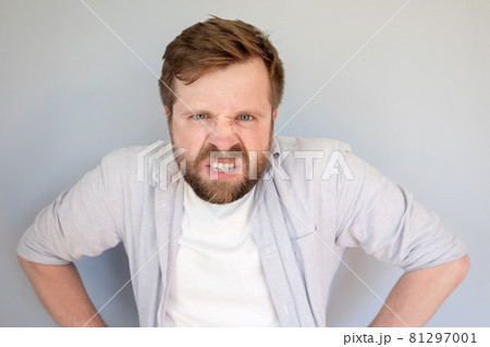 Caucasian bearded man is furious and displeased, he bares his teeth and looks angrily. Gray Caucasian bearded man is furious and displeased, he bares his teeth and looks angrily. Gray 81297001