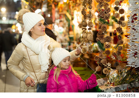 Smiling female and her daughter are choosing decorations for Christmas tree in the market outdoor 81300858
