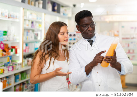 Young woman studies the composition of shampoo with a male pharmacist 81302904