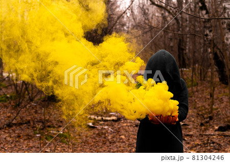 A creepy witch holds a steaming pumpkin in a deep forest. Jack o lantern emits yellow smoke for halloween 81304246