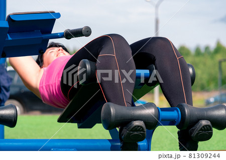 young woman shakes her press using an outdoor exercise machine abdominal bench young woman shakes her press using an outdoor exercise machine abdominal bench 81309244
