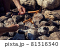 Human hands holding a sausage on a skewer and roasting it over a fire outdoor 81316340
