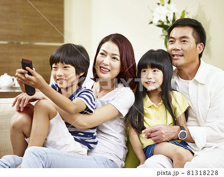 happy asian family with two children sitting on couch at home watching TV 81318228