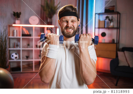 Man lifting dumbbells during evening time at home Man lifting dumbbells during evening time at home 81318993