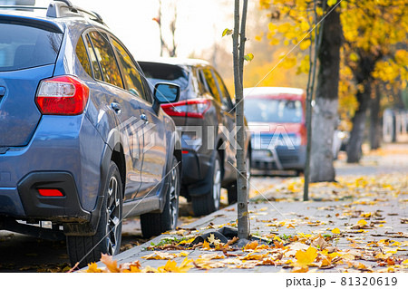 Cars parked in a row on a city street side on bright autumn day. 81320619
