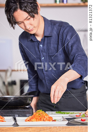 トマトパスタにパセリをかけるエプロン姿の若い男性　料理男子イメージ 81321372