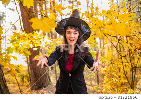 witch making magic. woman in a witch costume laughs and throws leaves to the camera in the autumn forest. halloween celebration 81321966