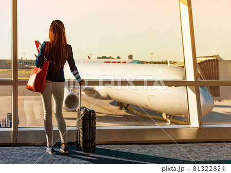 Travel during coronavirus pandemic tourist with luggage watching sunset at airport window. Unrecognizable woman waiting in lounge at boarding gate before departure. Travel lifestyle Travel during coronavirus pandemic tourist with luggage watching sunset at airport window. Unrecognizable woman waiting in lounge at boarding gate before departure. Travel lifestyle 81322824