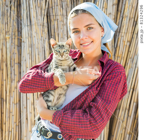 Smiling young female farmer holding tabby kitten in hands 81324296