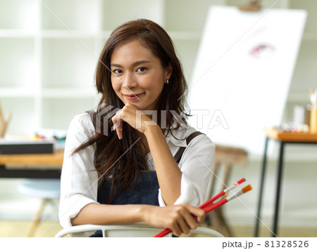 Beautiful asian female artist image, holding painting brushes, sitting, hand on chin Beautiful asian female artist image, holding painting brushes, sitting, hand on chin 81328526