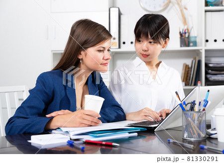 Businesswomen discussing over laptop at desk Businesswomen discussing over laptop at desk 81330291