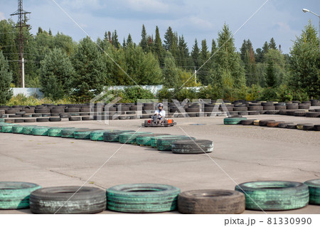 A girl or a woman in a hard hat rides a go-kart on a special track fenced with rubber wheels. Active recreation and sports on transport. Preparation and training for competitions.  81330990