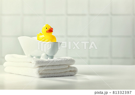A miniature bubble bath, yellow rubber duck and white towels on bathroom countertop, children bath accessories, baby care 81332397