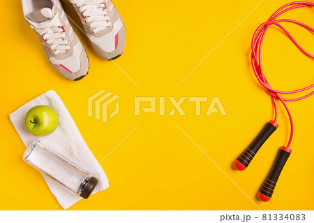 Athlete's set with female clothing, skipping rope and bottle of water on yellow background 81334083