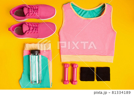 Fitness accessories on yellow background. Sneakers, bottle of water, dumbbells and sport top. 81334189
